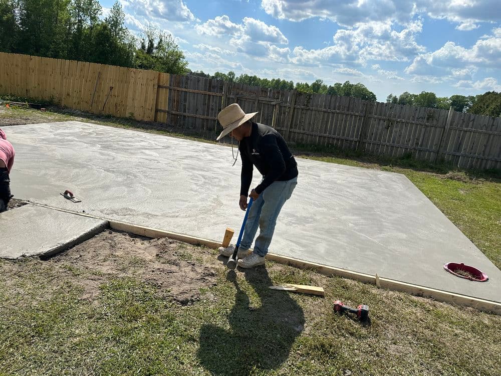 worker leveling concrete slab outdoors with tools and wooden forms, sunny sky in background