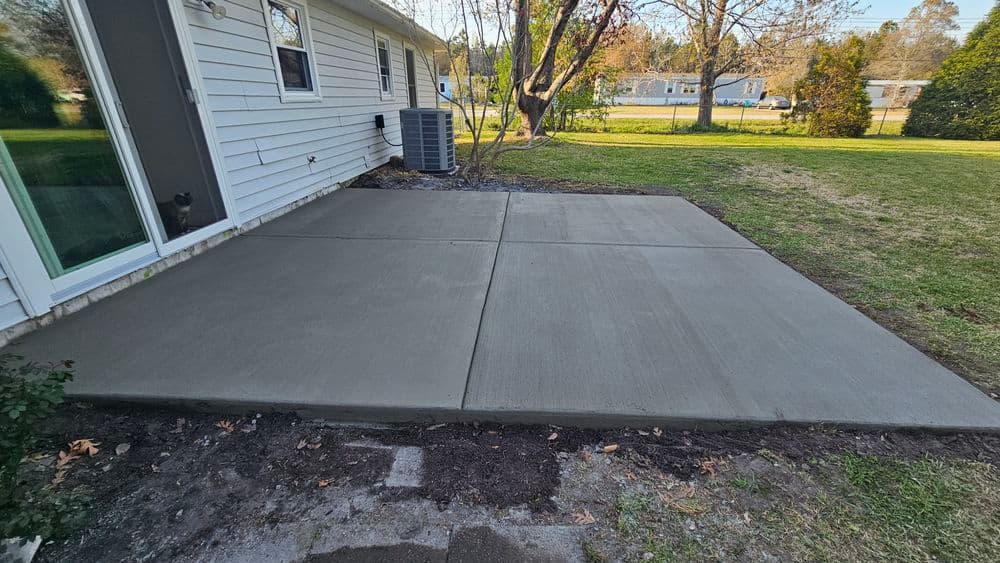 Newly poured concrete patio next to a house, featuring a clean finish and green lawn.