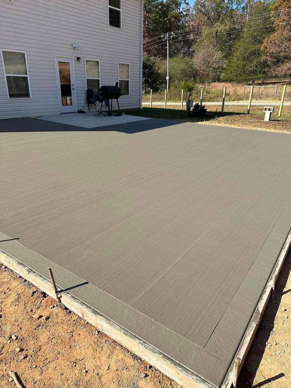 Freshly poured concrete patio with a smooth, gray surface, surrounded by a lawn.