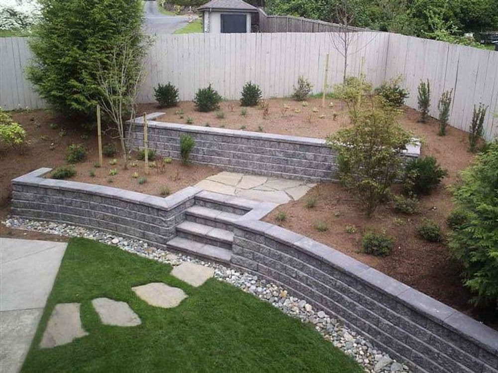 Landscaped backyard with stone retaining walls, steps, and plants surrounded by a wooden fence.