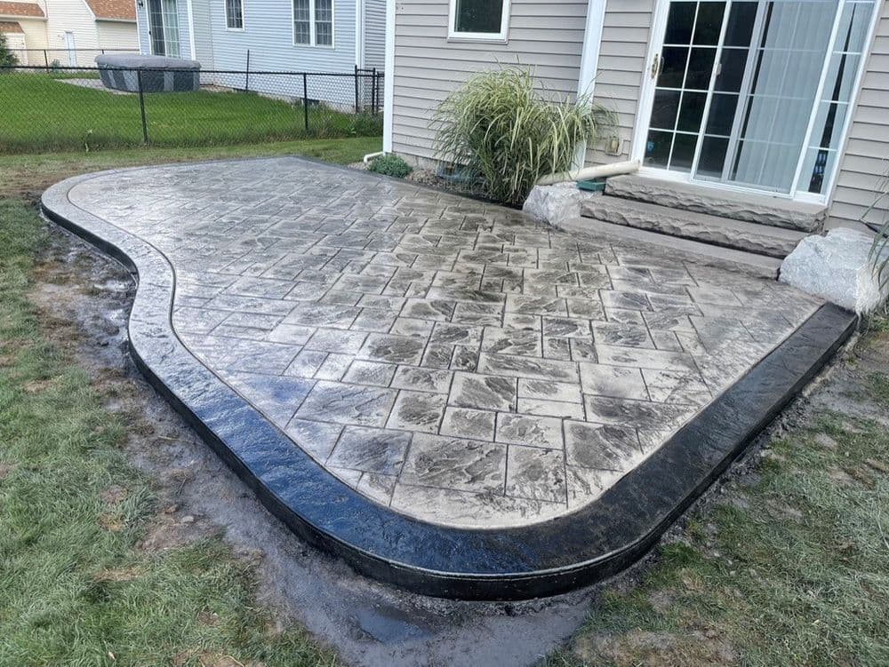Stamped concrete patio with black border, freshly installed beside a house and lawn.