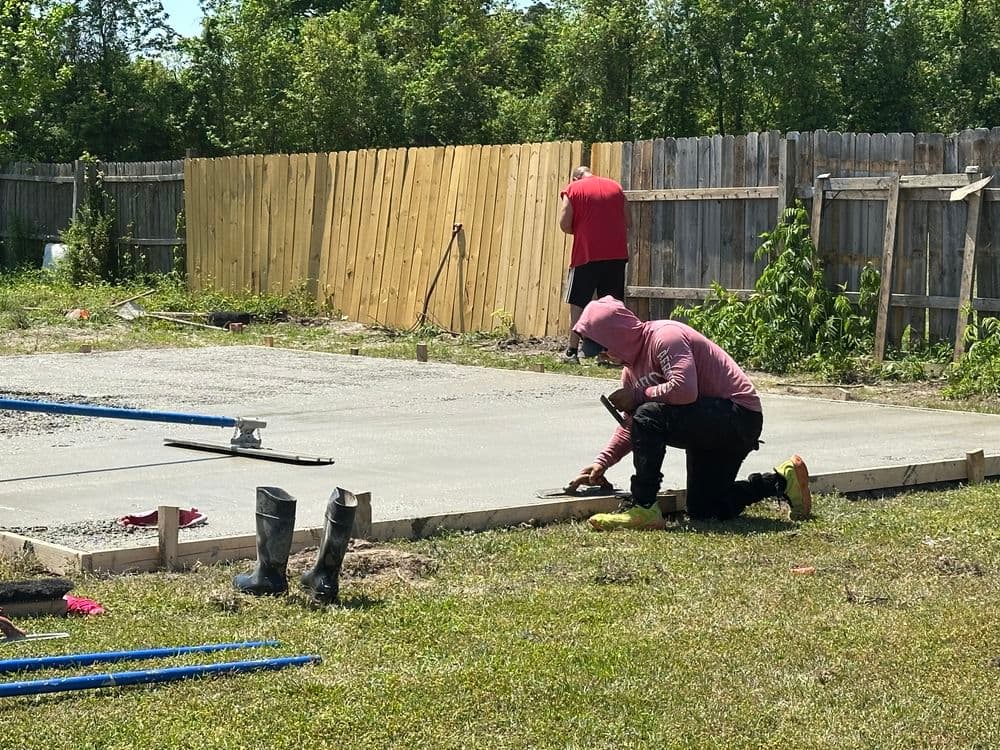 Construction workers leveling concrete for a foundation with tools and safety gear in a grassy area.