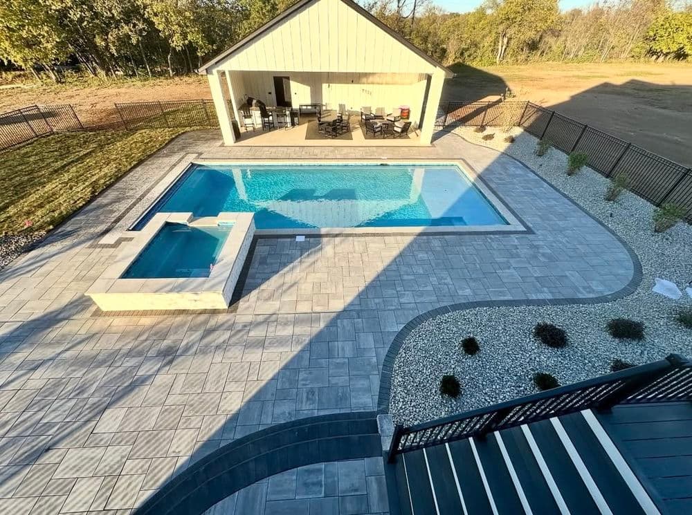 Modern backyard pool with spa, surrounded by patio and landscaped garden, near a covered seating area.