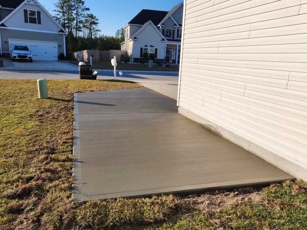 Freshly poured concrete slab next to a residential home in a suburban neighborhood.