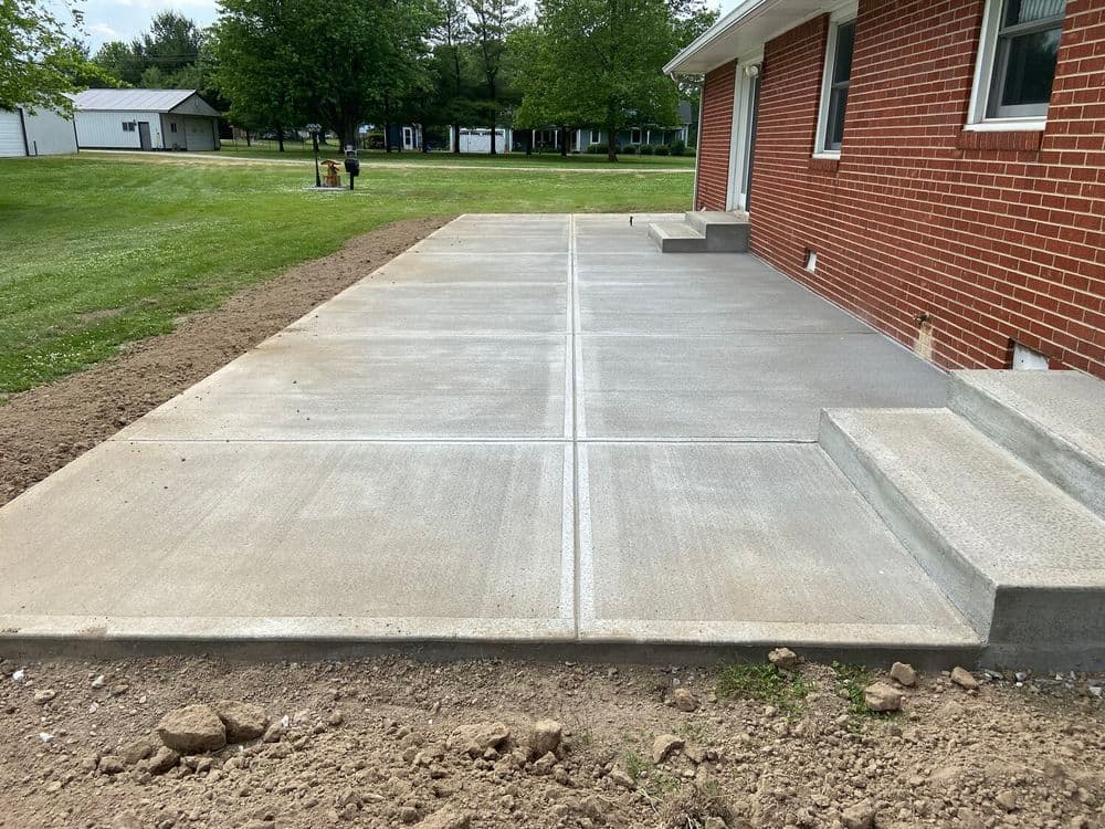Newly poured concrete patio with steps, surrounded by grass and landscaping.