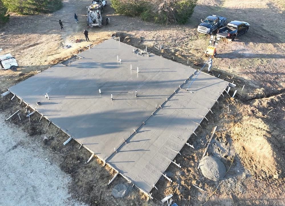 Aerial view of workers pouring concrete for a foundation on a construction site.