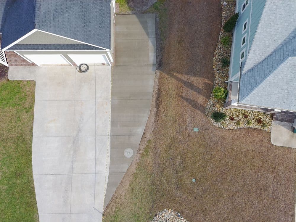 Aerial view of driveway and landscaping beside a house with green siding.