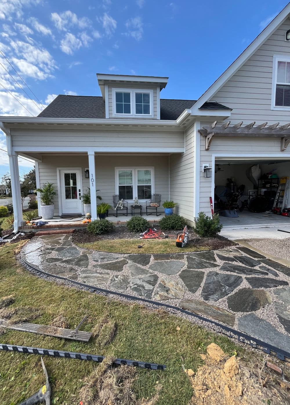 Modern home facade with stone walkway, porch seating, and garage entrance.
