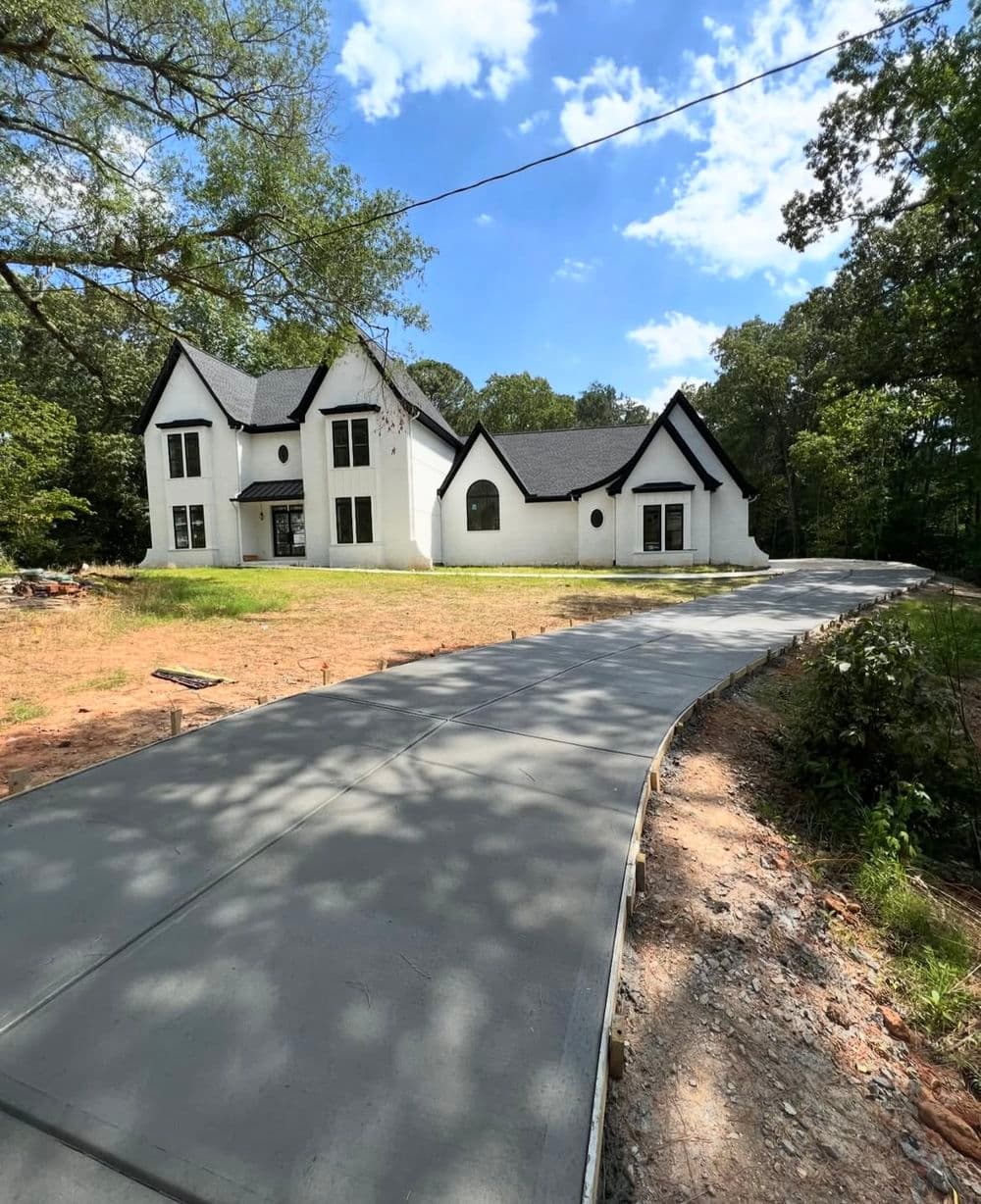 Newly constructed white modern house with a curved concrete driveway surrounded by trees.