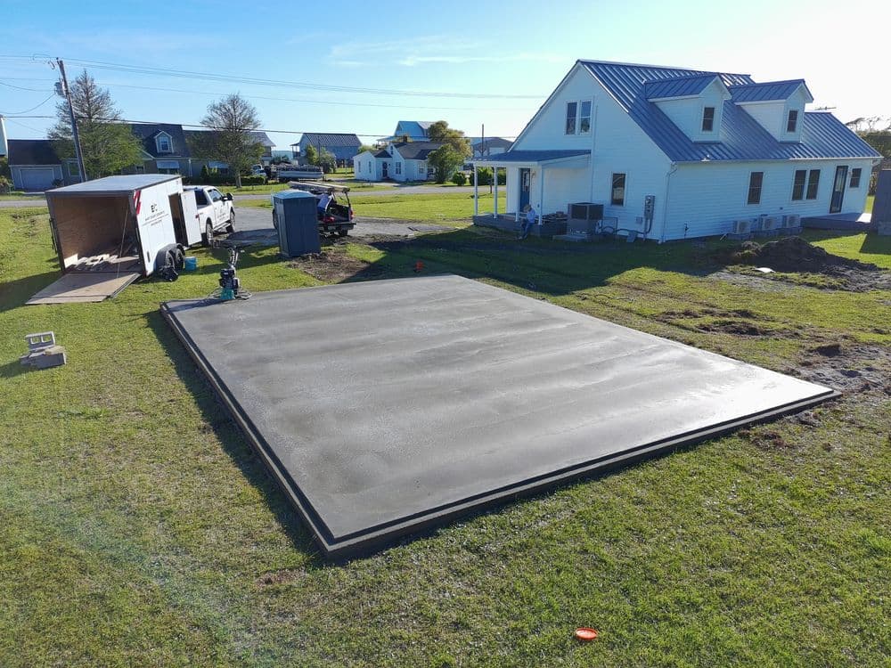 Concrete slab foundation prepared for construction beside a house in a rural setting.