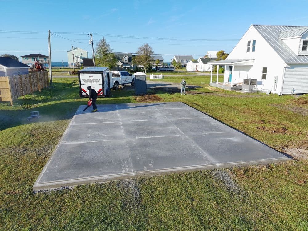 Concrete slab being poured on a residential property, with workers and equipment on-site.