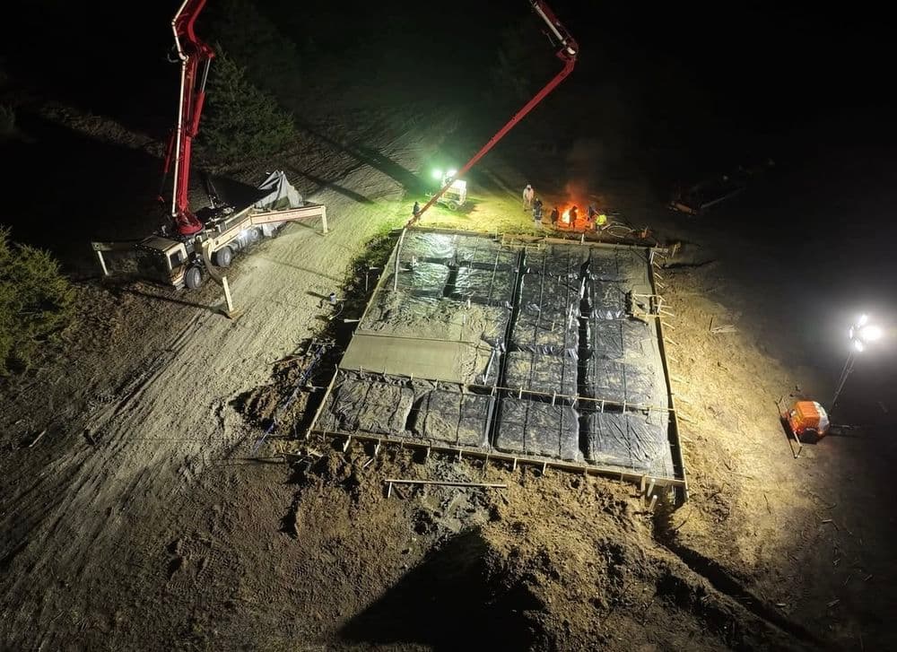 Construction site at night with concrete pouring and workers around equipment.