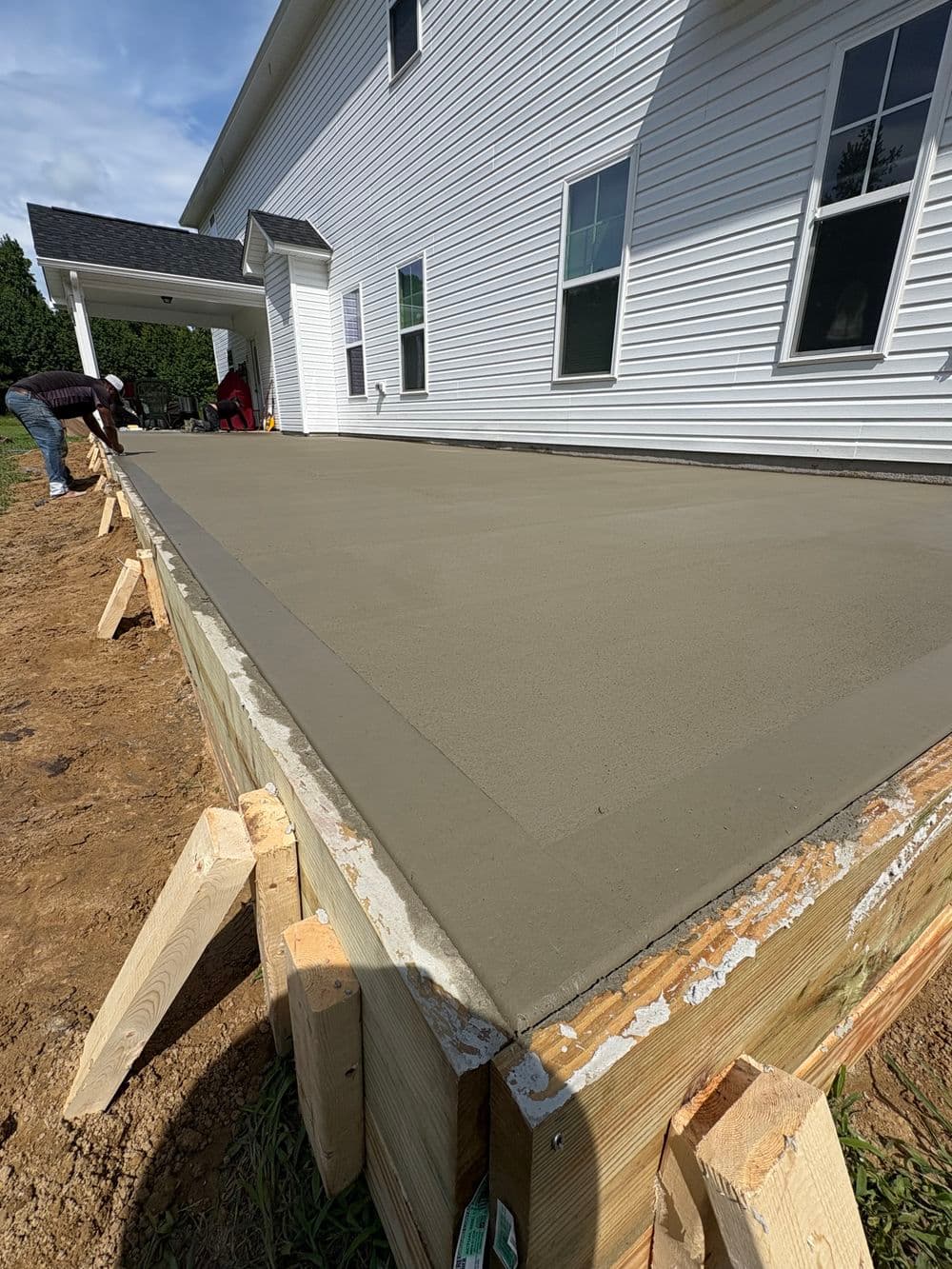 Newly poured concrete slab for a house addition, surrounded by wooden forms and construction workers.