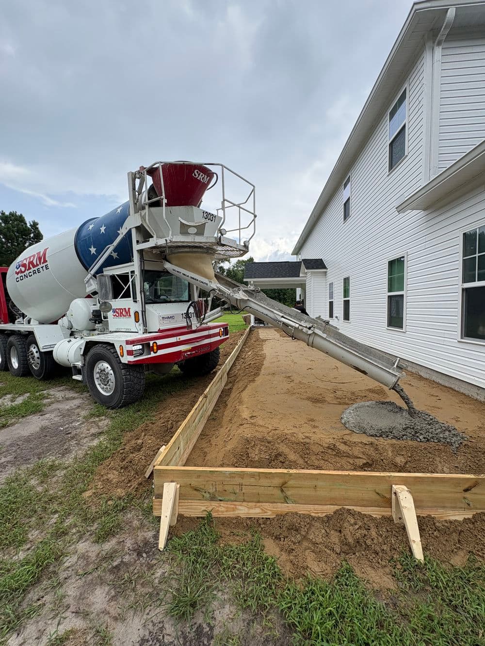 Concrete mixer truck pouring concrete into wooden frame for a driveway installation.