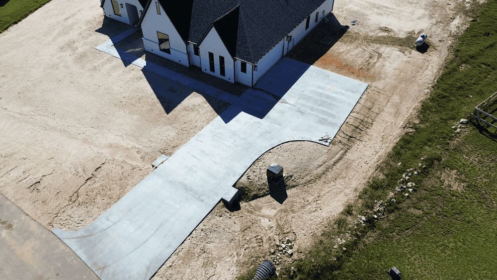 Aerial view of a newly poured concrete driveway beside a modern home under construction.
