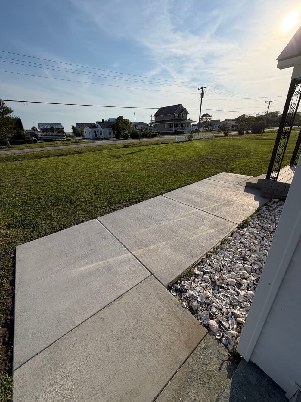 Concrete sidewalk leading to a home with grassy lawn and coastal houses in the background.