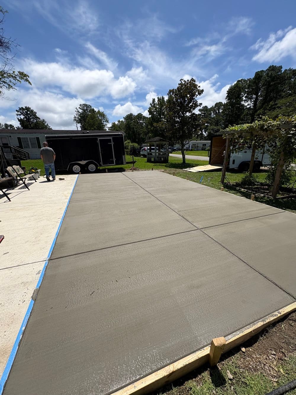 Freshly poured concrete slab for a parking area with a trailer and nearby trees.