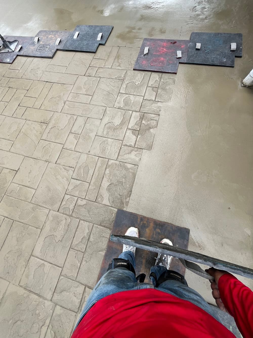 Person standing on mats while finishing stamped concrete patio. Wet surface and tools visible.