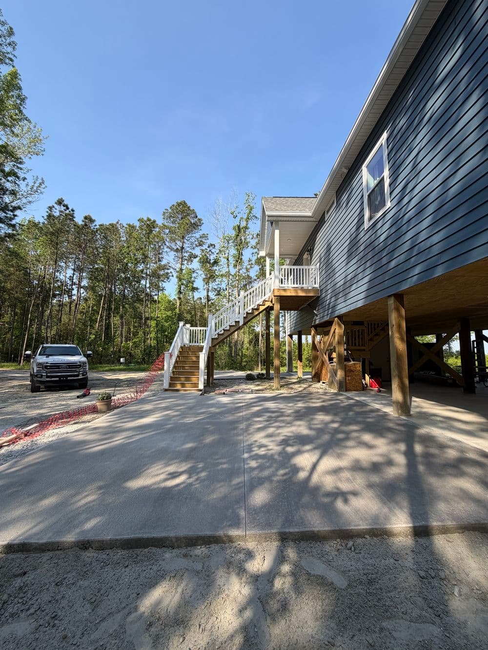 Newly constructed house with wooden stairs and driveway, surrounded by trees.