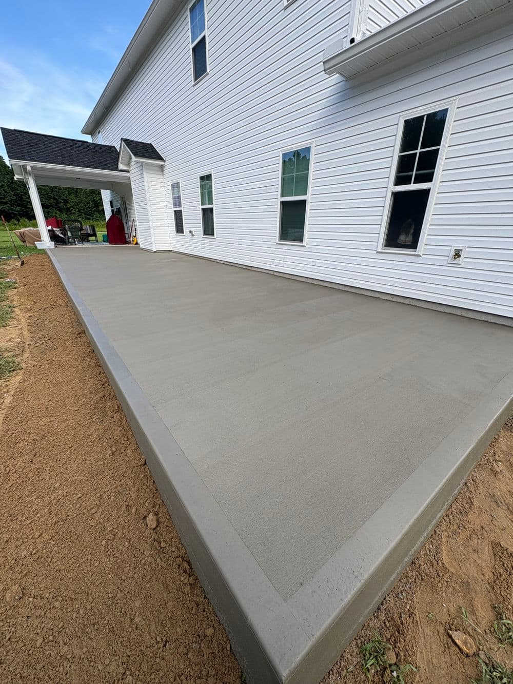 Freshly poured concrete patio beside a white house with large windows and a covered entryway.