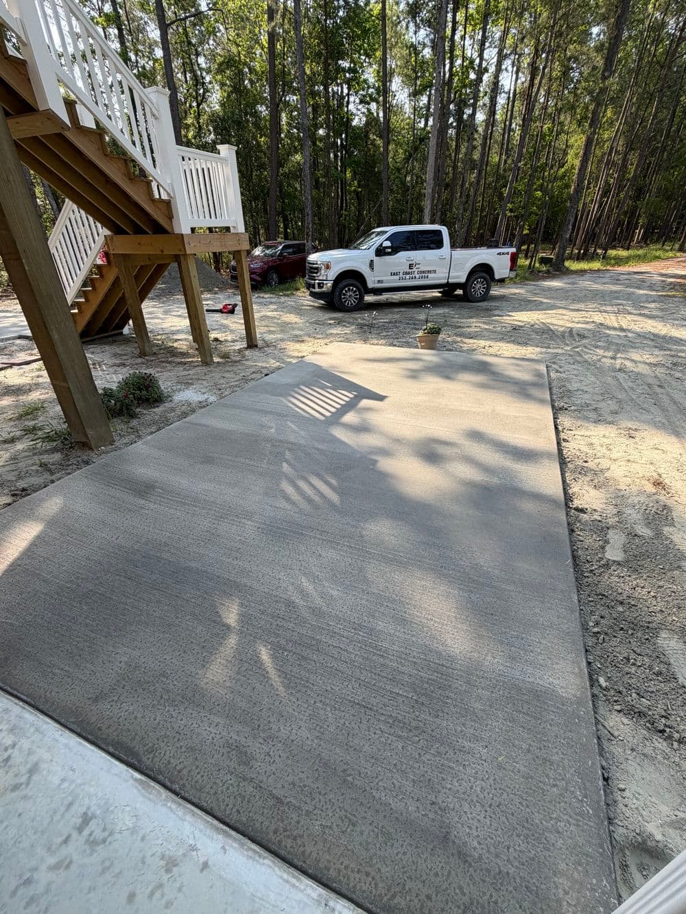 Freshly poured concrete driveway with a pickup truck parked nearby and trees in the background.