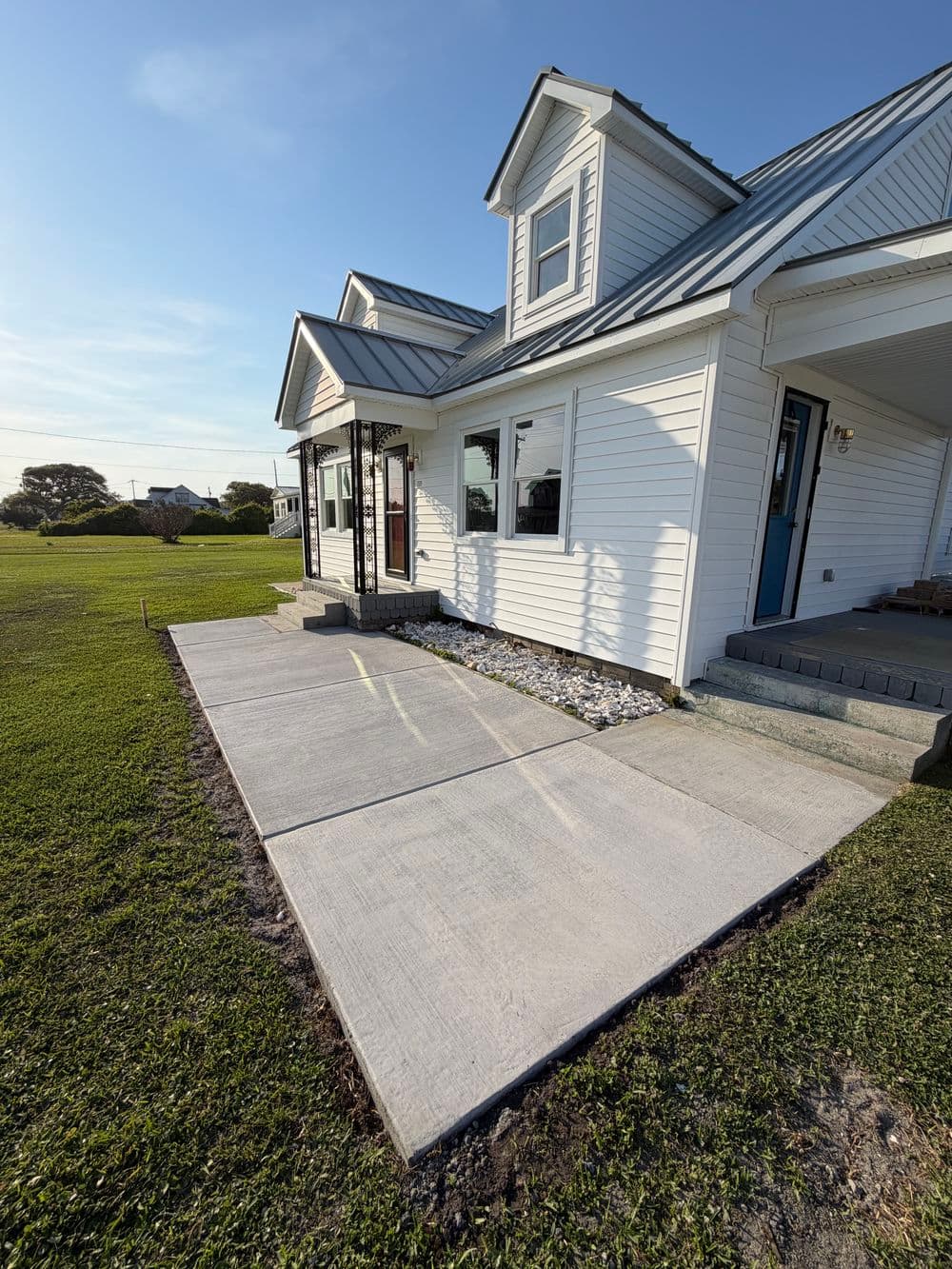 Modern white house exterior featuring new concrete walkway and landscaped grass yard.