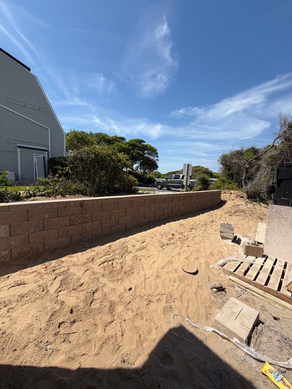 Construction scene with a retaining wall, sand, and a truck in a coastal landscape.