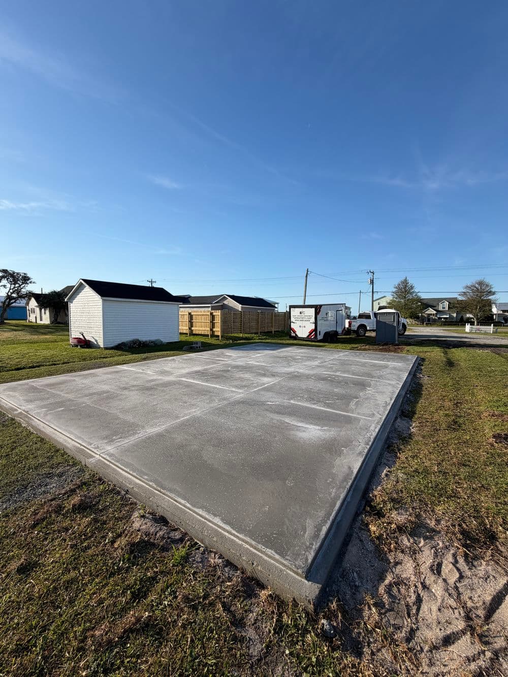 Concrete foundation slab ready for construction, surrounded by grass and utility buildings.