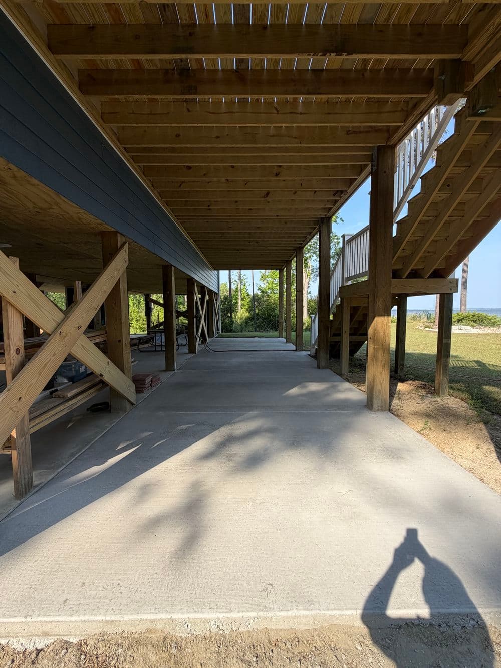 Covered outdoor space under wooden structure with concrete flooring and stairs.