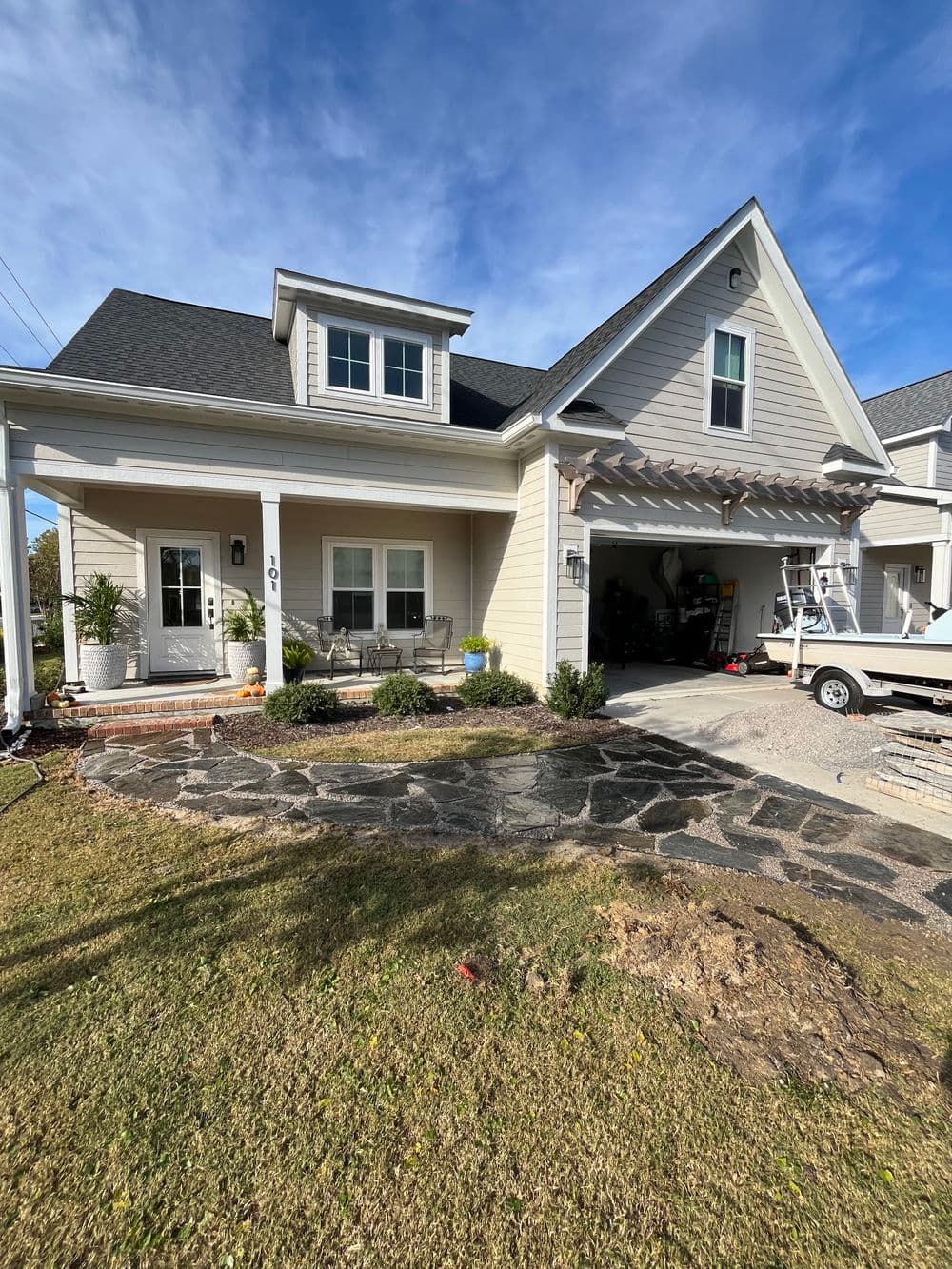 Modern two-story home with a porch, landscaped yard, and driveway leading to a garage.