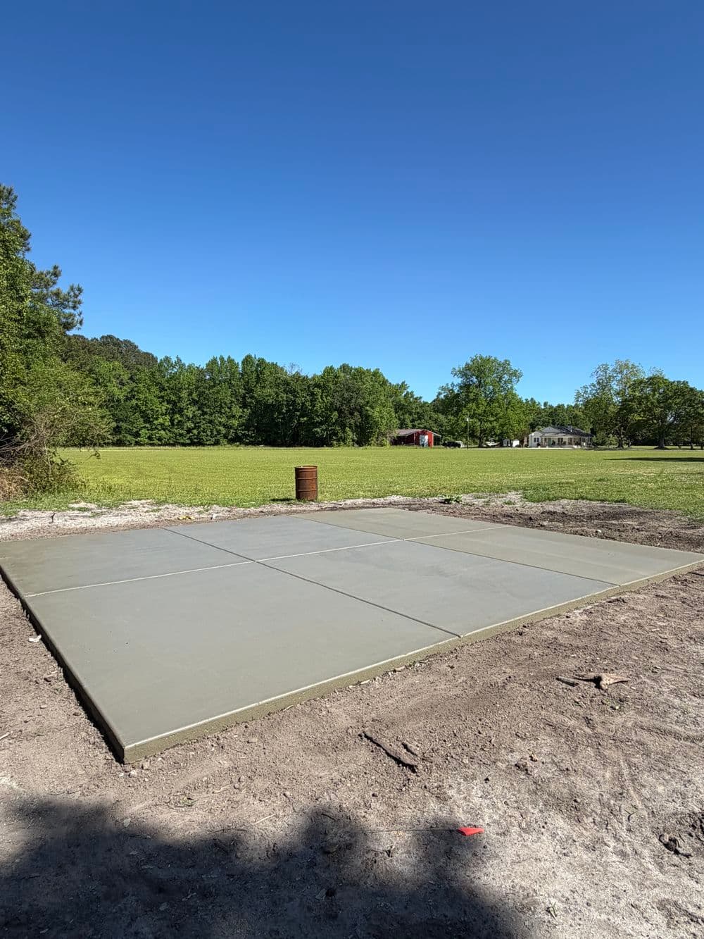 Freshly poured concrete slab on a grassy lot under a clear blue sky. Ideal for construction.