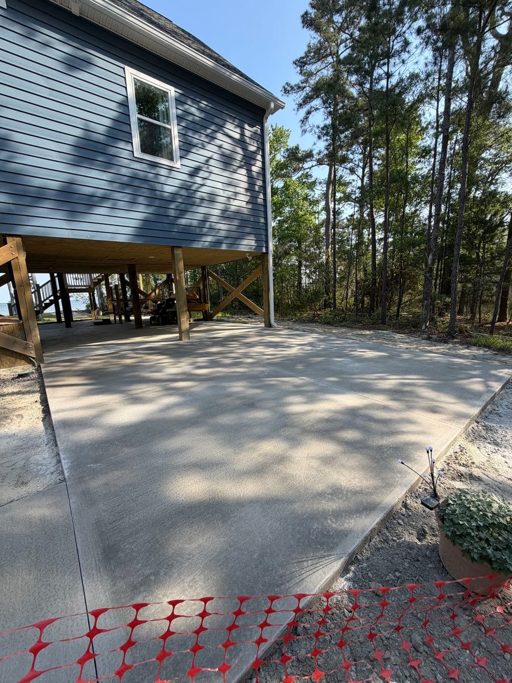 Freshly poured concrete driveway beside a blue house, surrounded by trees.
