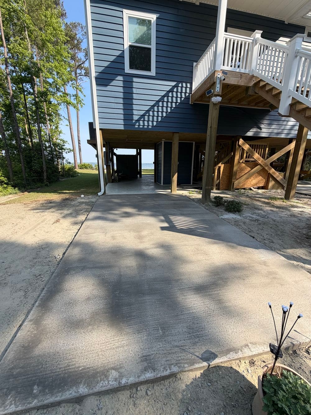 Driveway leading to a blue house with a covered area and trees in the background.