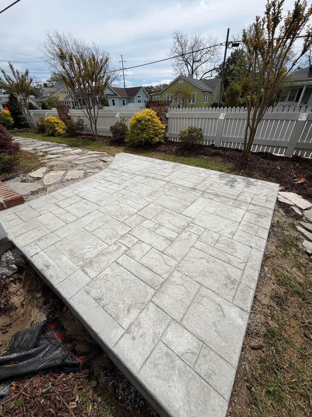 Newly installed stamped concrete patio with intricate patterns, surrounded by landscaping.