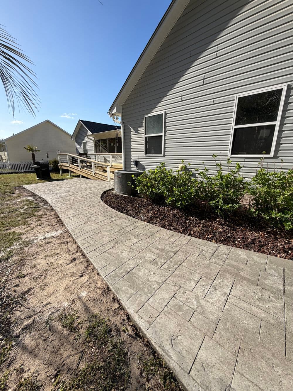 Curved stone pathway leading to a house with greenery and blue sky in the background.