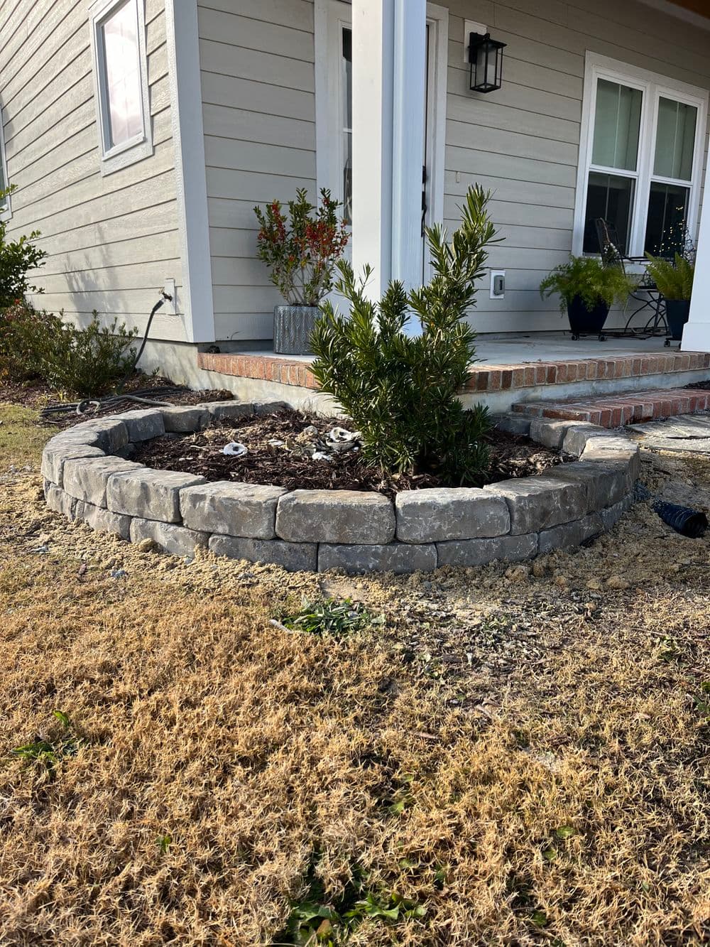 Stone garden bed featuring a central plant and landscaped with brown mulch outside a home.