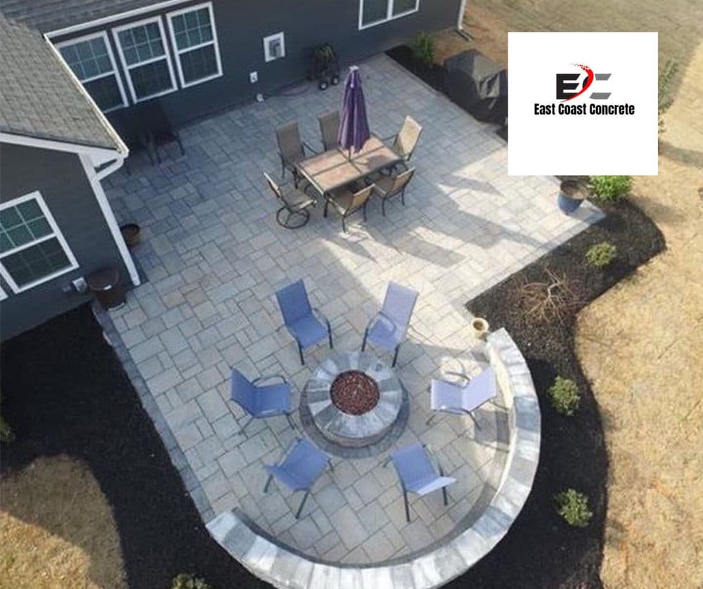 Backyard patio with stone seating, fire pit, dining set, and landscaping by East Coast Concrete.
