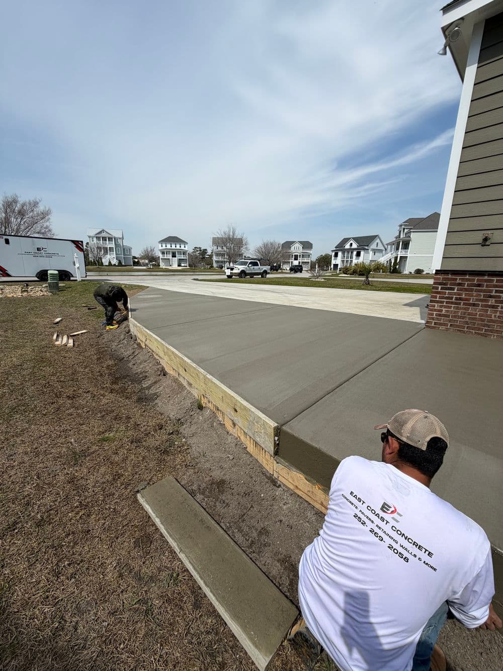 Workers pouring concrete for a driveway installation in a residential area.
