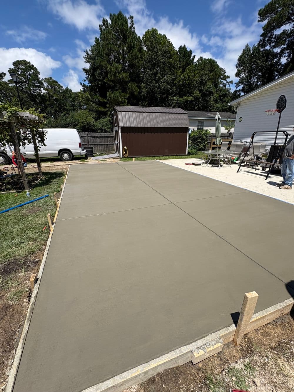 Freshly poured concrete slab in a backyard with trees and a storage shed in the background.