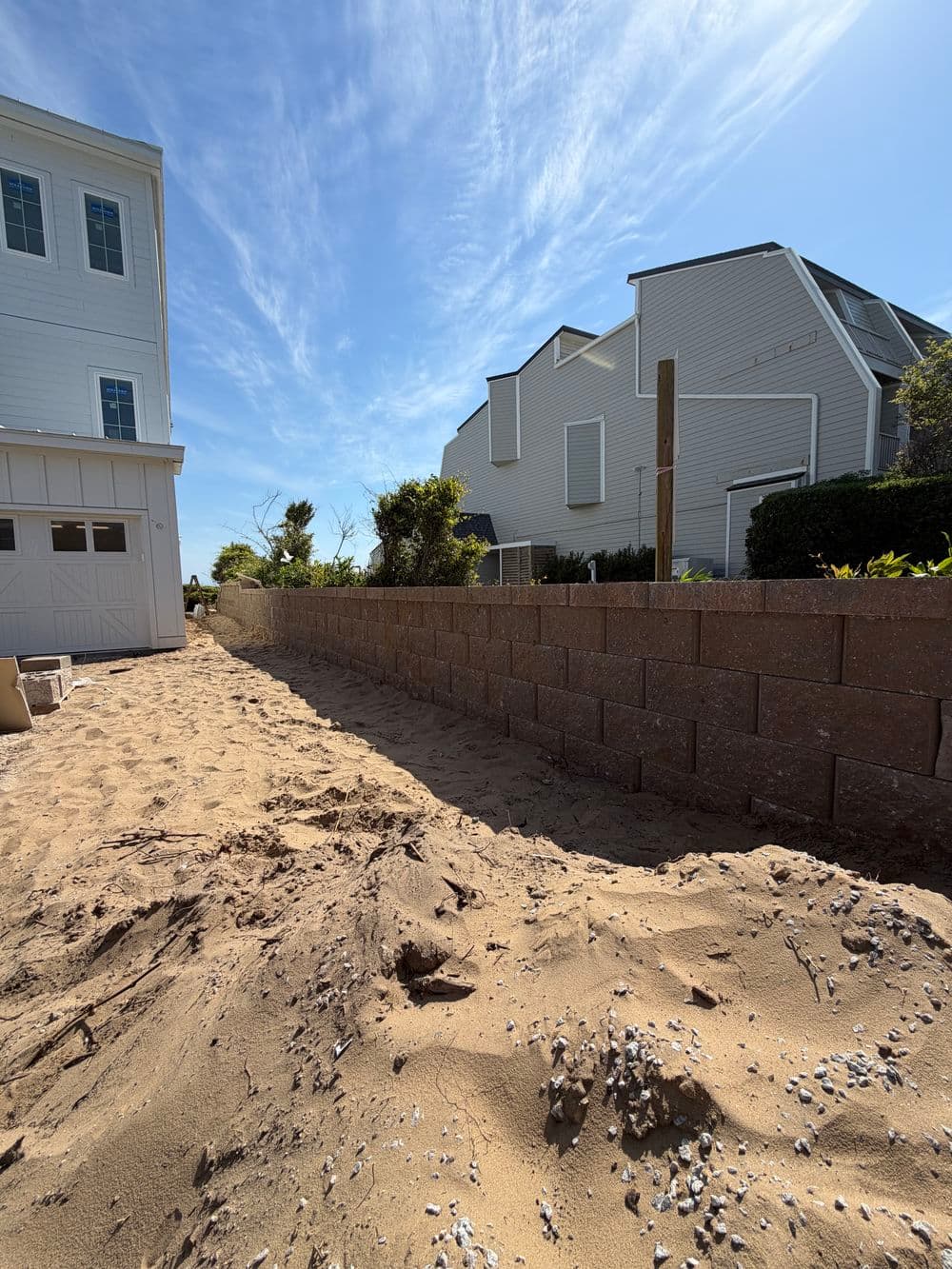 Construction site showing a sand-filled area beside a house and a concrete block wall.