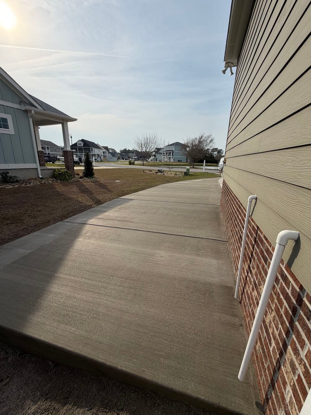 Concrete walkway leading to a house, with a spacious yard and houses in the background.
