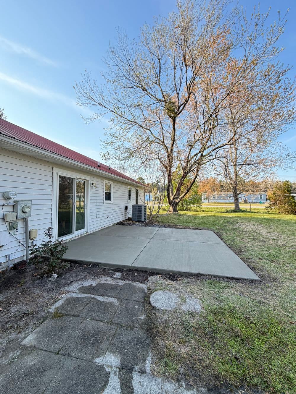 Patio area with new concrete slab beside a house, tree in background, sunny day.