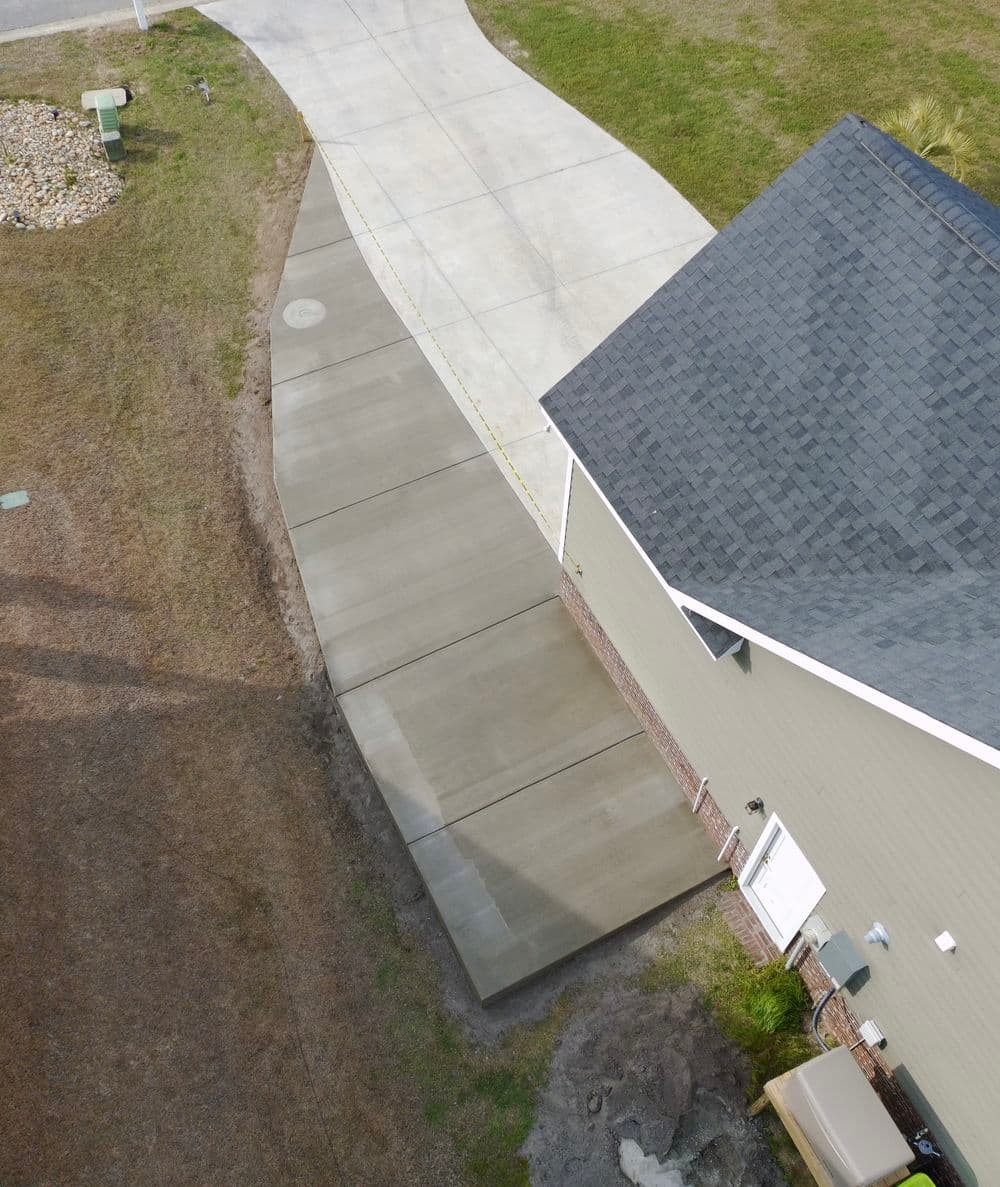 Aerial view of a residential driveway leading to a beige house with a dark roof.