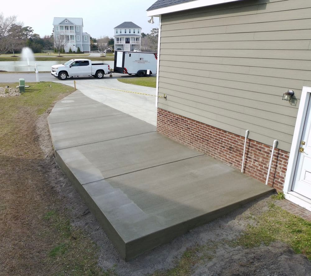 Newly poured concrete driveway extension beside a residential home with landscaping.
